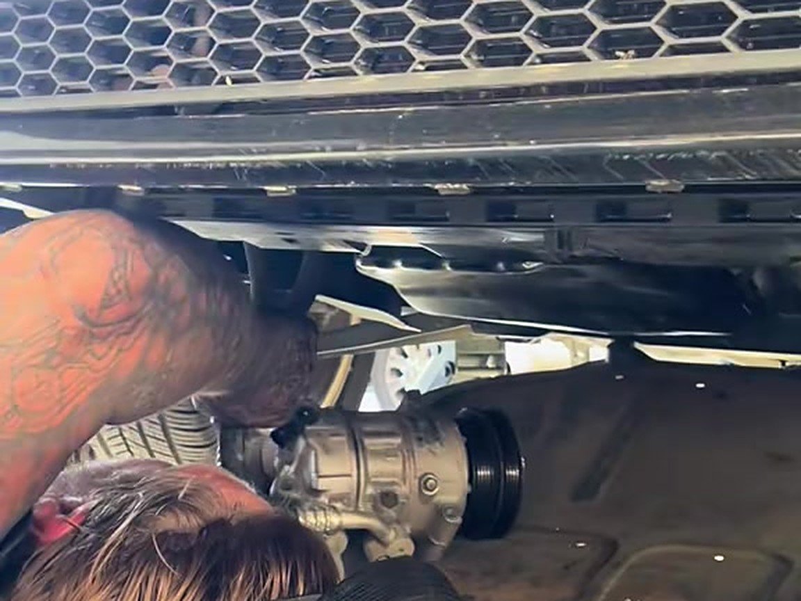 Mechanic lying under the front of a vehicle, fitting a part from below during an alternator install