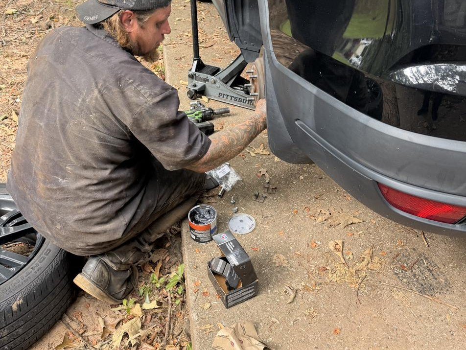 Mobile mechanic replacing brake pads on an SUV in a customer's driveway