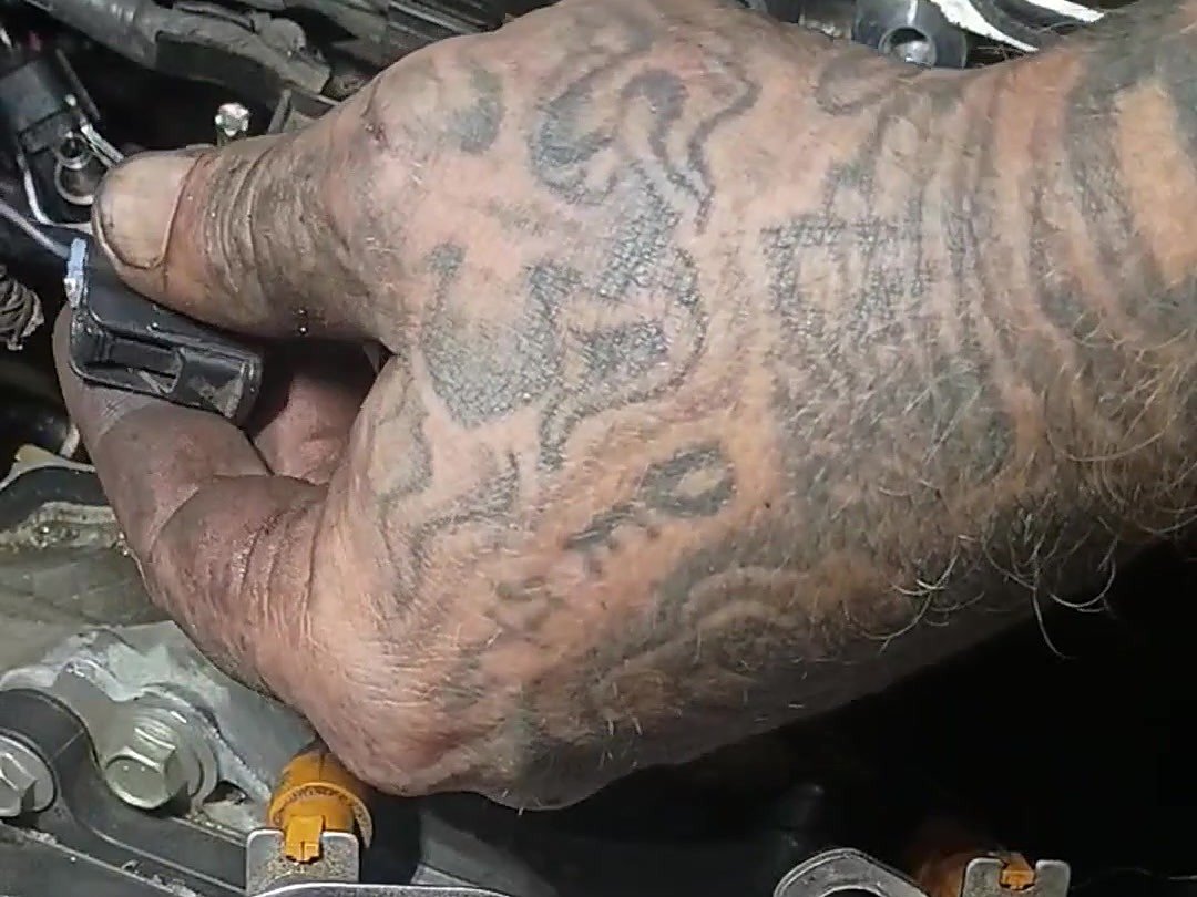 Mechanic's hand holding a wiring connector on an engine with the intake removed