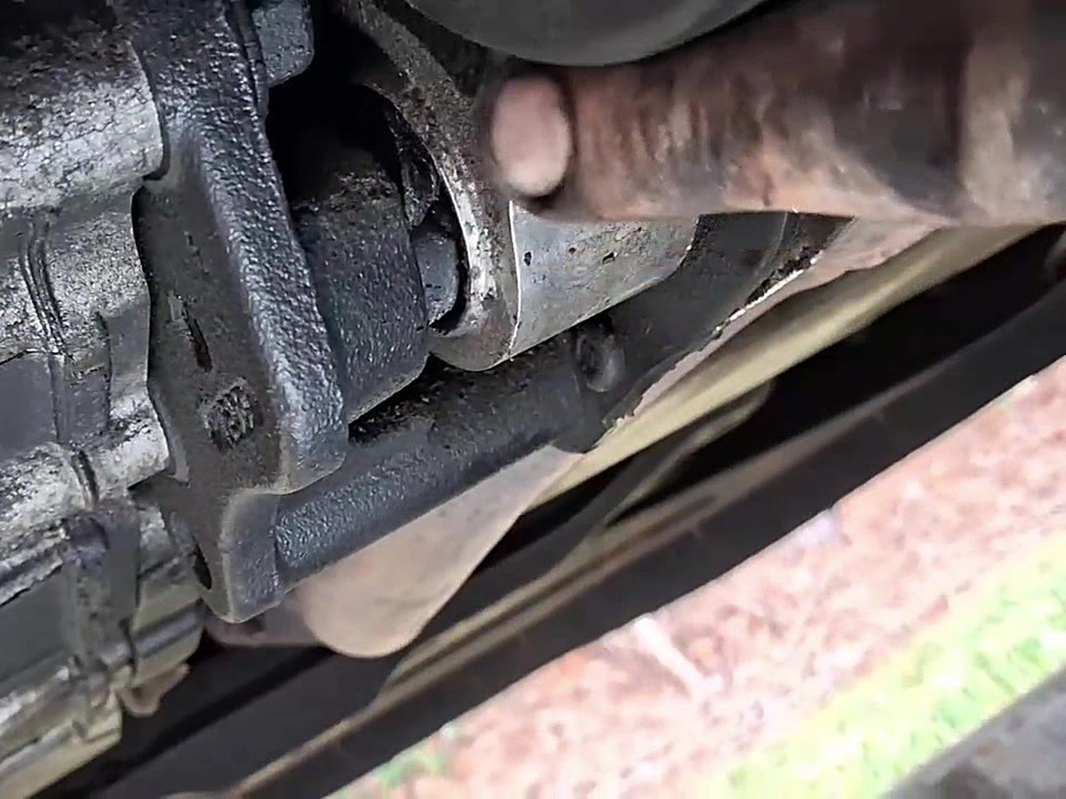 Mechanic's finger pointing at a motor mount, seen from under the vehicle